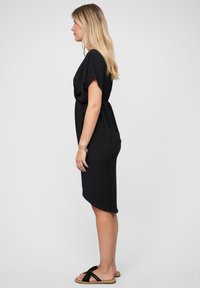 Black knee-length dress with short sleeves, textured fabric, fitted waist, and a slightly curved hem. Paired with flat sandals.