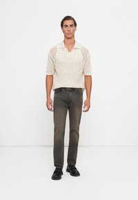 Világos bézs kötött pólóing rövid ujjakkal; sötét szürke farmernadrággal párosítva. A modellen fekete slip-on cipők vannak. Egyszerű, modern dizájn.