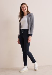 Navy en witte gestreepte cardigan met een strakke witte top, gecombineerd met navy joggers en witte sneakers. Eenvoudig ontwerp, casual stijl.