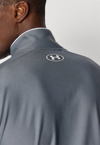 Gray athletic shirt with a structured collar, featuring a textured fabric and a white logo on the back. Minimalist design and modern fit.