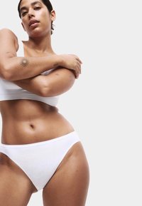 Bela pamučna bralette i bikini set, s glatkom teksturom, niskim strukom i minimalnim šavovima, nošen na neutralnoj pozadini.