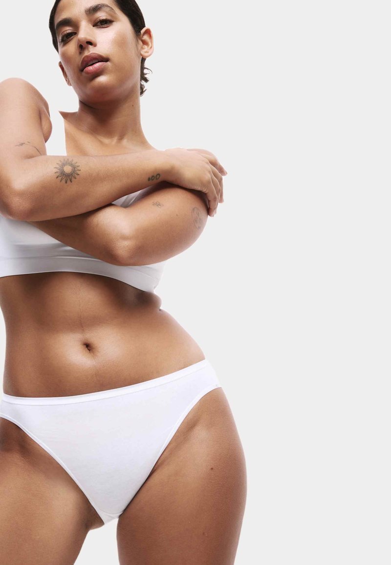 Bela pamučna bralette i bikini set, s glatkom teksturom, niskim strukom i minimalnim šavovima, nošen na neutralnoj pozadini.