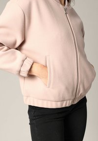 Lichtroze zip-up jack gemaakt van zachte stof, met zijzakken, geribbelde manchetten en een ontspannen pasvorm aan de onderkant.