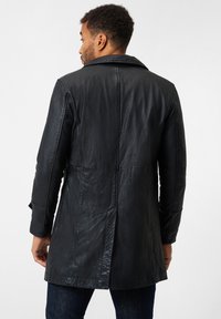 Zwarte leren jas met een gestructureerde afwerking, met een ingesneden kraag, lange mouwen en een middellange snit. De achterzijde toont naaddetails.