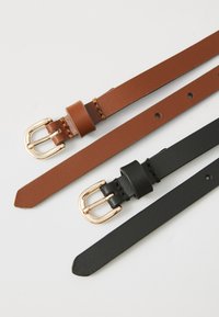Deux ceintures en cuir, l'une marron et l'autre noire, avec des boucles en métal doré sur un fond blanc.