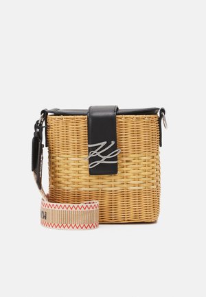 Sac bandoulière rectangulaire en osier tressé avec rabat en cuir noir et logo argenté, bandoulière beige avec couture zigzag rouge.