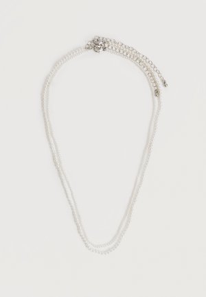 Collier de perles double rang avec rallonge de chaîne en argent et fermoir mousqueton sur fond blanc.