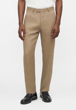 Beige skræddersyede bukser med forreste pres, bæltestropper, båret med sorte læder loafers og en hvid indstukket skjorte.