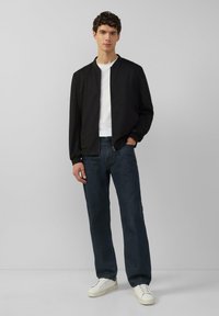 Zwarte bomberjack, witte crewneckshirt eronder, donkerblauwe jeans en witte sneakers. Eenvoudig ontwerp, gecombineerd met neutrale kleuren.