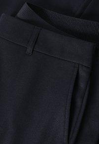 Tissu bleu marine avec une finition texturée, présentant une ceinture plate et des détails plissés. Le matériau semble lisse et durable.