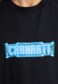 Camiseta de algodón negra con un diseño gráfico digital azul. El texto aparece en letras en bloque con un efecto pixelado.