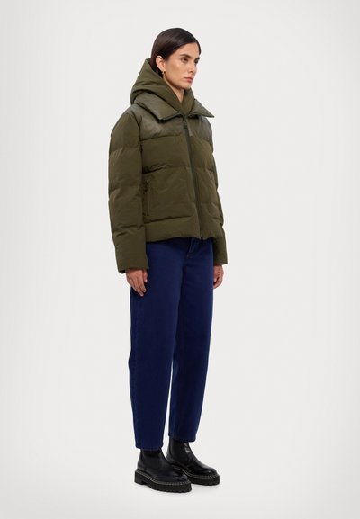 Mörkgrön quiltad pufferjacka med hög krage och stor huva, kombinerad med blå denimjeans och svarta plattformstövlar.