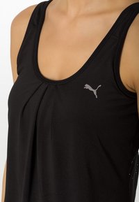 Top negro sin mangas hecho de tela suave, con un pliegue en la parte frontal y un pequeño logo gris de Puma en el pecho izquierdo.
