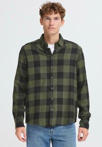Camicia in flanella a quadri verdi e neri, design con bottoni, maniche lunghe, texture morbida, con colletto e dettagli di cucitura visibili.