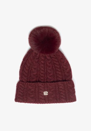 Burgundská pletená čepice s copánkovým vzorem, ohrnutým lemem, malým kovovým logem a velkým načechraným bambulí na vrchu.