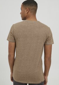 Ruda trumpa rankovė t-shirt su subtiliu tekstūruotu raštu, apvaliu iškirpimu ir stilingais siūlais. Medžiaga atrodo lengva ir minkšta.