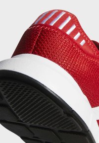 Czerwony but sportowy z teksturowaną cholewką z tkaniny, białą podeszwą i czarną gumową bieżnią z geometrycznym wzorem.