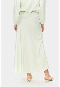 Satin maxi seelik helesinis, voolava disainiga, sile tekstuur ja veidi laienev äär. Lisavarustusena heledate kollaste kingadega.