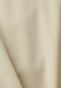 Tissu beige clair avec une texture lisse visible dans les plis et les ombres douces.