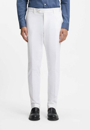 Białe, dopasowane spodnie o prostym kroju, wykonane z lekkiego materiału. Posiadają gładki przód i boczne kieszenie, zestawione z czarnymi mokasynami.