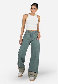 Vit ribbad crop top i kombination med vida blå jeans, som har en vikta, kontrasterande fåll. Sneakers fulländar outfiten.