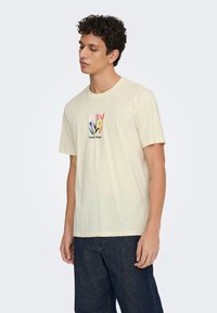 Ανοιχτόκκινο βαμβακερό t-shirt με κοντά μανίκια, με φλοράλ γραφικό σε ροζ, μωβ, κίτρινο και πορτοκαλί, και κείμενο από κάτω.