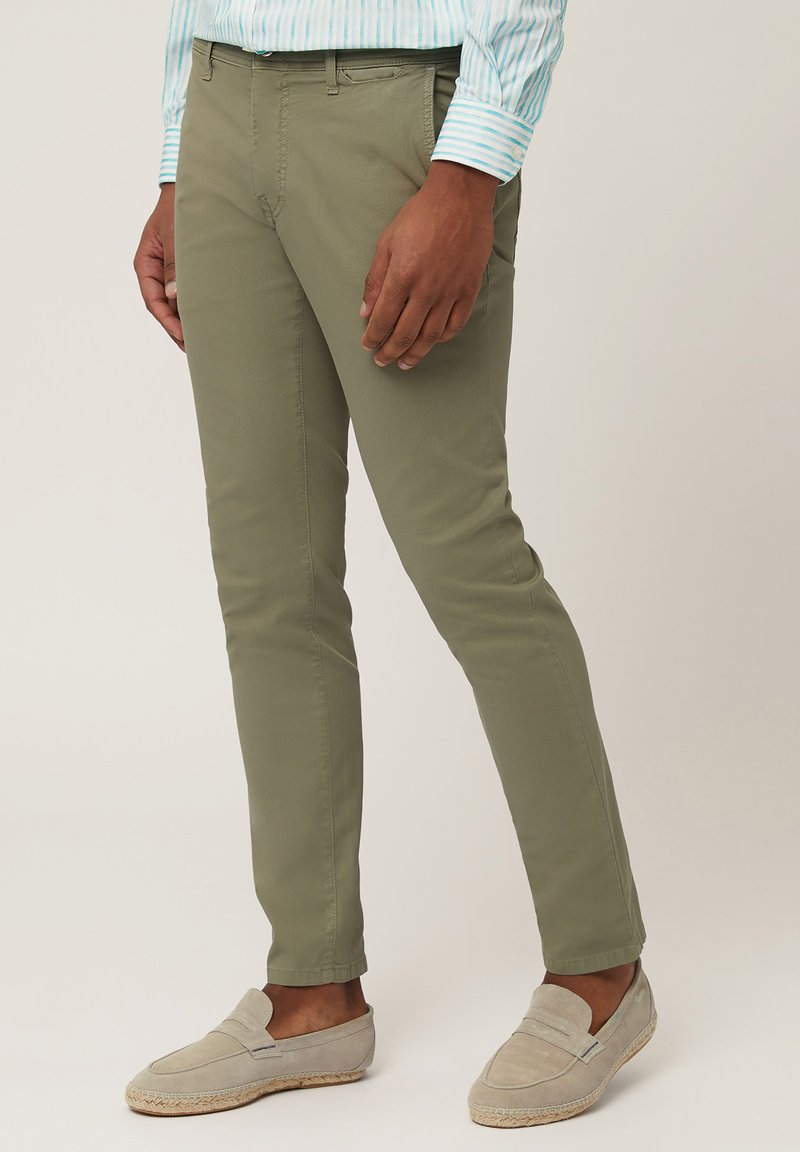 Olive green chinos made of cotton with a slim fit, flat front, and side pockets, paired with gray slip-on shoes.