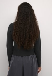 Pulover din lână gri închis, cu mâneci lungi, ce prezintă un talie ajustată și o textură moale, asortat cu o fustă fluidă închisă pentru contrast.