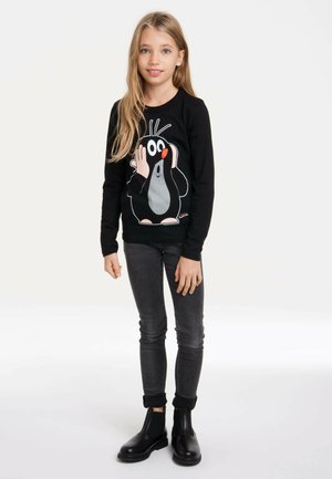 Schwarz langärmliges Shirt mit einem Cartoon-Maulwurf-Design, kombiniert mit grauen engen Jeans und schwarzen Stiefeletten. Einfaches, lässiges Outfit.