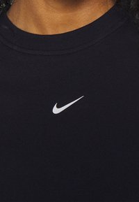 Musta puuvillainen T-paita pyöreällä kaula-aukolla, jossa on pieni valkoinen Nike-logo rinnassa. Pehmeä materiaali ja rento istuvuus.