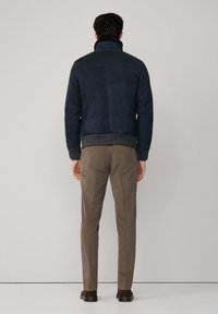 Mornarska suknja od zamšene kože s visokim ovratnikom, rebrastim manžetama i rubom. Uparen s bež hlačama i tamnosmešnim cipelama, prikazan s leđa.