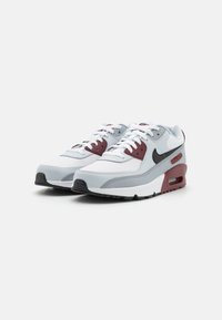 Os sapatilhas Nike Air Max 90 apresentam um cabedal em branco, cinza e bordeaux, com materiais de couro e malha, solado grosso e detalhes em preto.