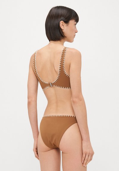 Rudas bikini su baltais siuvinėjimais. Viršus turi plačias juostas ir apačioje yra iškirpta dizaino; apatinė dalis turi aukštą iškirpimą. Lygus paviršius.