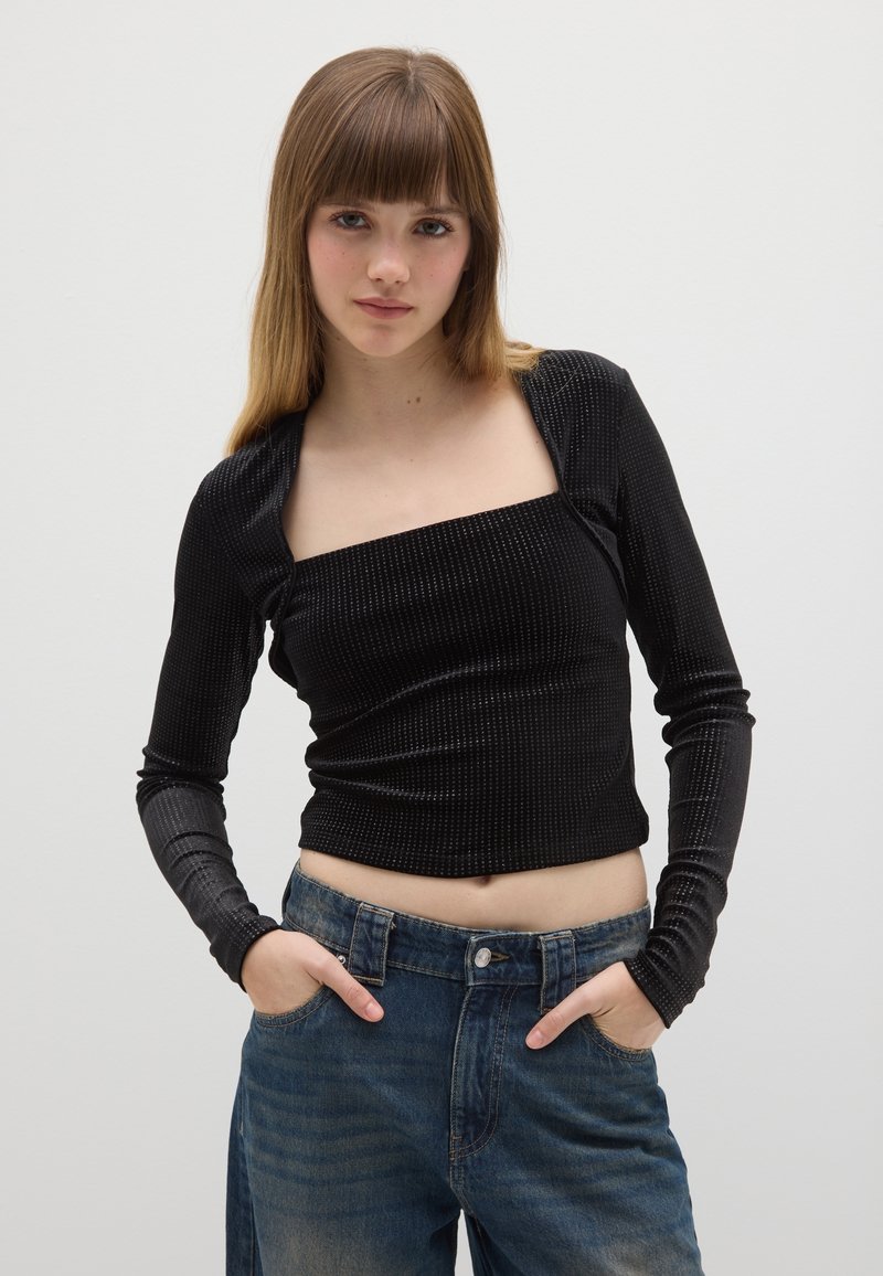 Schwarzes Langarmoberteil mit quadratischem Ausschnitt, geripptem Muster und figurbetontem Schnitt, kombiniert mit hoch taillierten blauen Jeans aus Denim.