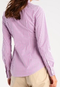 Pruhovaná košile ve světle fialové a bílé barvě, s límcem na knoflíky, dlouhými rukávy a bílými knoflíky na manžetách.