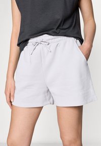 Pantalones cortos de mezcla de algodón de color gris claro con cintura elástica, cordón ajustable, bolsillos laterales y detalle impreso de "ATHLEISURE" en el dobladillo.