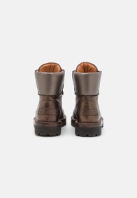 Stivali alla caviglia metallici marroni con texture liscia, colletto imbottito e suole robuste. Presentano un logo del marchio in rilievo sul tallone.
