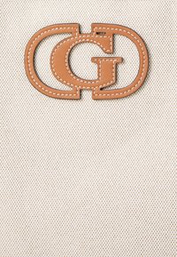 Beige stof med en struktureret overflade, der har et brunt læderapplikationslogo formet som sammenflettede "G" og "D" med hvide syninger.