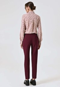 Blusa rosa a maniche lunghe con motivo floreale, abbinata a pantaloni sartoriali color bordeaux e scarpe platform nere. Outfit visibile da dietro.