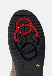 Zwarte rubberen zool met drie rode cirkelvormige elementen, uitgerust met metalen studs en een gestructureerd grippatroon. Merken zichtbaar aan de zijkant.