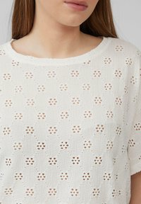 Witte T-shirt met korte mouwen, voorzien van een textuur en reliëfpatroon met openingen. Ronde halslijn met een licht rafelige rand.