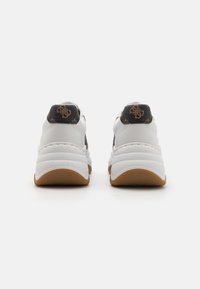 Zapatillas blancas con un talón negro texturizado que presenta acentos de logo en relieve, una suela acolchada y una suela de goma para mayor agarre.