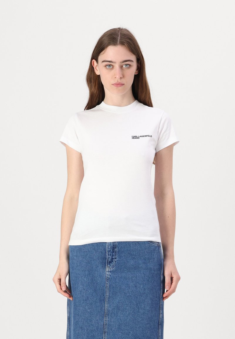 Witte katoenen t-shirt met korte mouwen en een hoge ronde hals. Bevat een klein zwart logo op de linkerkant van de borst. Gepaard met een spijkerrok.