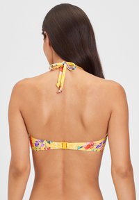 Bikini-top met bloemenpatroon in geel, met een halternek-tie en een haaksluiting op de rug. Glad textuur, levendige kleuren van roze, paars en groen.