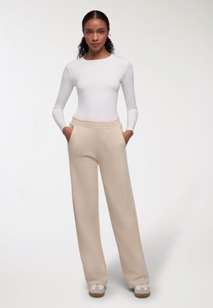 Top bianco a maniche lunghe abbinato a pantaloni beige a gamba larga, con vita elastica e tasche laterali. Tessuto strutturato e vestibilità casual.