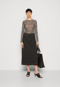 Transparente Langarmbluse mit Zebramuster, hoch taillierter dunkler Jeansrock mit fransigem Saum, schwarze Absatzmules und eine schwarze Tragetasche.