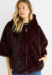 Burgundy faux fur jacket featuring a hood, diagonal black stripes, zip closure, and dropped shoulders. Soft texture with side pockets.