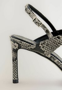 Sandalo con tacco alto caratterizzato da un motivo in pelle di serpente nera e grigia, con una sottile fascia alla caviglia e una superficie testurizzata.
