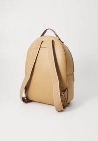 Brauner Leder-Rucksack mit runder Form, verstellbaren Trägern, die mit dem prägierten Markennamen versehen sind, und einem Reißverschlussverschluss. Glatte Textur, minimalistisches Design.