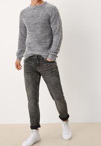 Grauer Strickpullover mit rundem Ausschnitt, kombiniert mit schwarzen, ausgeranzten Jeans und weißen High-Top-Sneakers. Texturiertes Material, lockere Passform.